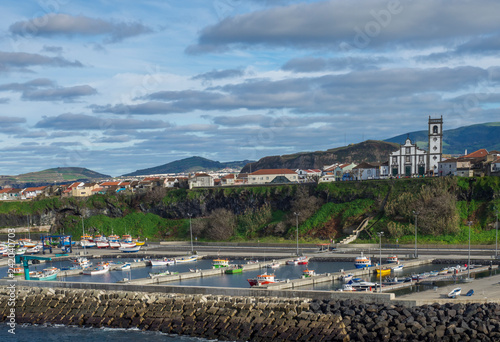 View of colorful quay and port of village Rabo de Peixe with boats, church and houses in Sao Miguel, the largest of the Azores Islands, Portugal. Sunny cloudy day
