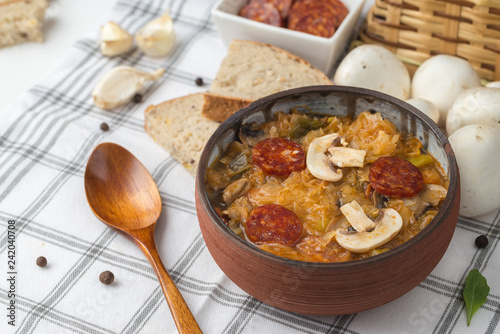 Slovak Christmas national cabbage soup in small black pot with sausage on the tablecloth background.