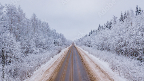 Aerial view of country road going through the beautiful snow covered landscapes.