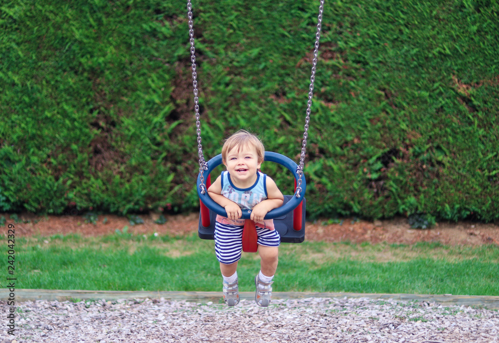 Cute happy smiling little child having fun riding on swing at children playground on summer day. Carefree childhood.