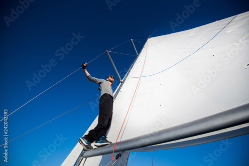 Handsome bearded man in sunglasses on a regatta standing on a sail boom