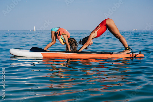 Mom and little daughter doing yoga on the paddle board