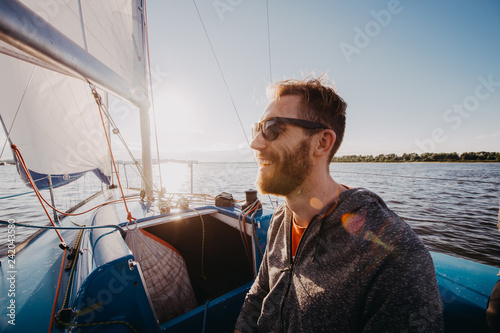 Man dressed in casual wear and sunglasses on a yacht. Happy adult bearded yachtsman close-up portrait. Handsome sailor on a boat smiling during regata on a sea or river.