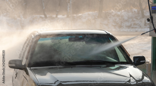 Spraying water from a high pressure hose to the side of a car at a self-service car wash