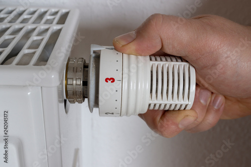 hand of man adjusting temperature on thermostat on radiator