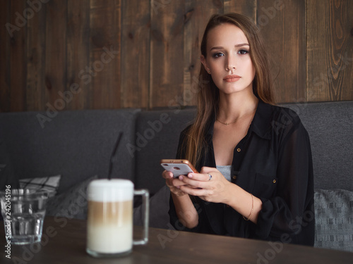 Beautiful woman reading good news on mobile phone during rest in coffee shop. Happy caucasian female watching photos on smartphone checking social networks while relaxing in cafe during free time