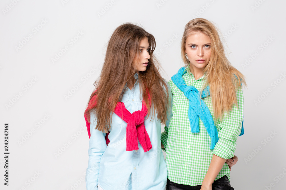 happy girlfriends women in shirts and a sweater on his shoulders. Fashion spring image of two sisters. Colorful colors clothes. Models with Blonde and light brown hair. Looking at camera . happy girlfriends women in shirts and a sweater on his shoulders. Fashion spring image of two sisters. Colorful colors clothes. Models with Blonde and light brown hair. Looking at camera .