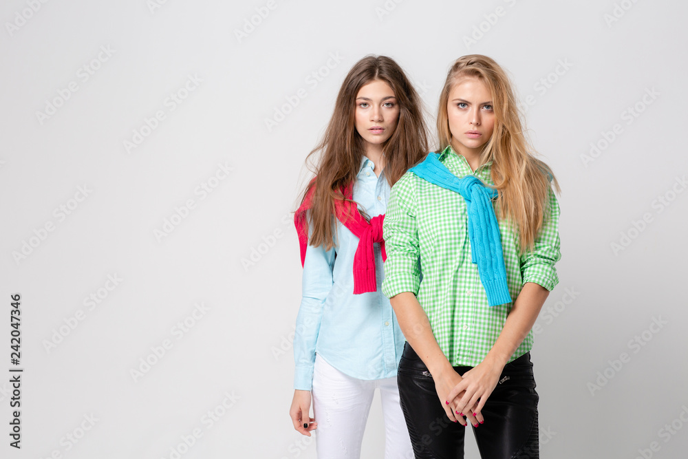 happy girlfriends women in shirts and a sweater on his shoulders. Fashion spring image of two sisters. Colorful colors clothes. Models with Blonde and light brown hair. happy girlfriends women in shirts and a sweater on his shoulders. Fashion spring image of two sisters. Colorful colors clothes. Models with Blonde and light brown hair.