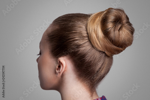 Profile side view closeup portrait of woman with creative elegant brown collected hairstyle, bun hair. indoor studio shot, isolated on grey background. photo