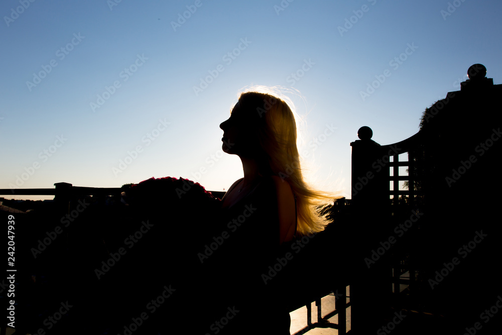 Young sexy blonde woman staying at balcony silhouette at sunset