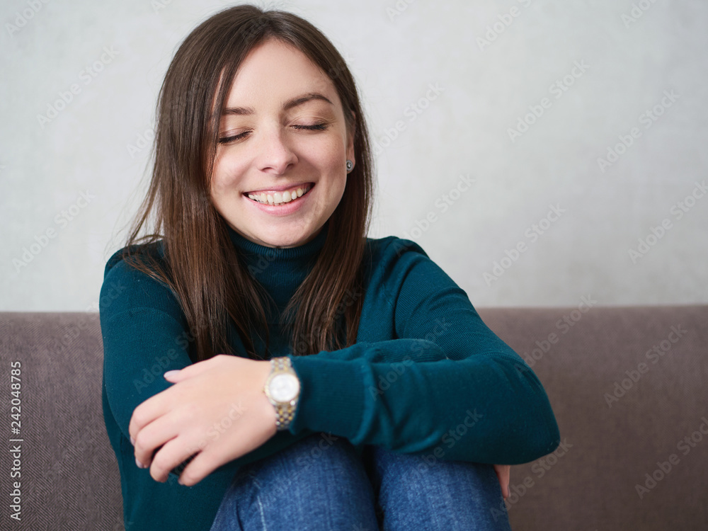 Pretty brunette woman with magnificent eyes and adorable smile in green sweater and blue jeans relaxing sitting on sofa at home Pretty brunette woman with magnificent eyes and adorable smile in green sweater and blue jeans relaxing sitting on sofa at home