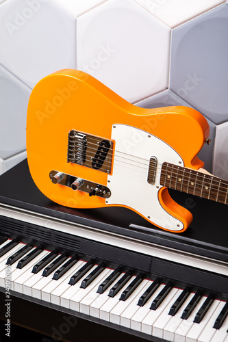 Orange electric guitar laying on piano, closeup