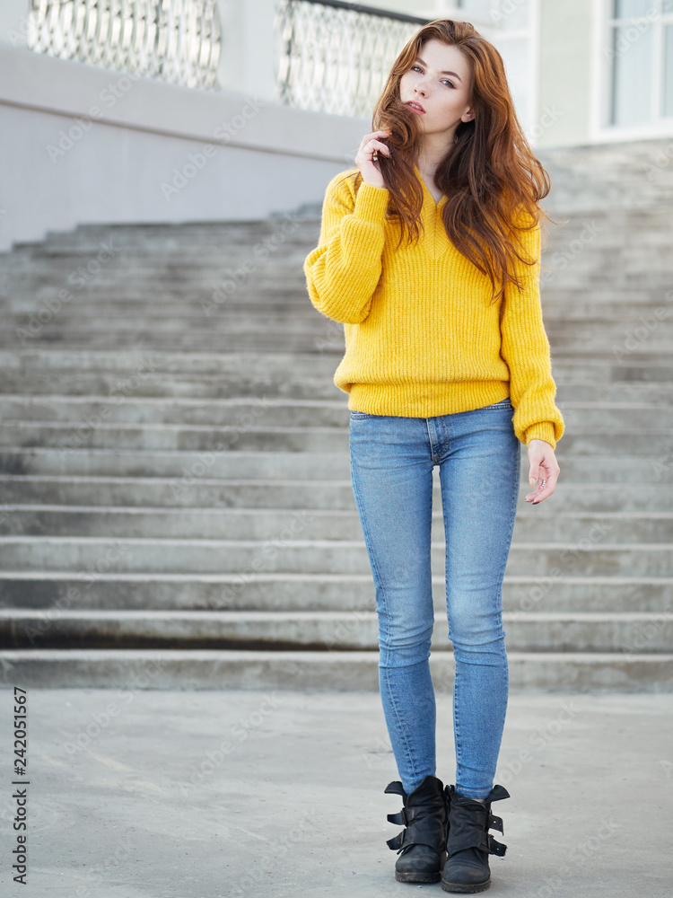 Full body shot of fabulous redhead woman with long hair in yellow sweater  having fun on grey concrete stairs background. Stock Photo | Adobe Stock