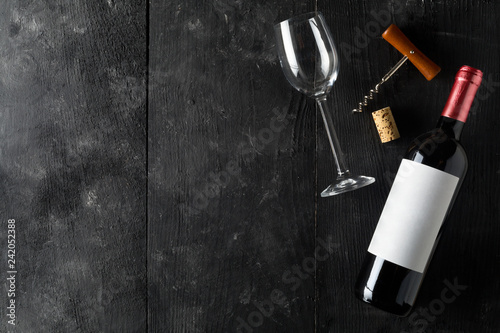 Red wine bottle with corkscrew, cork and wine glass on dark wooden table flat lay from above