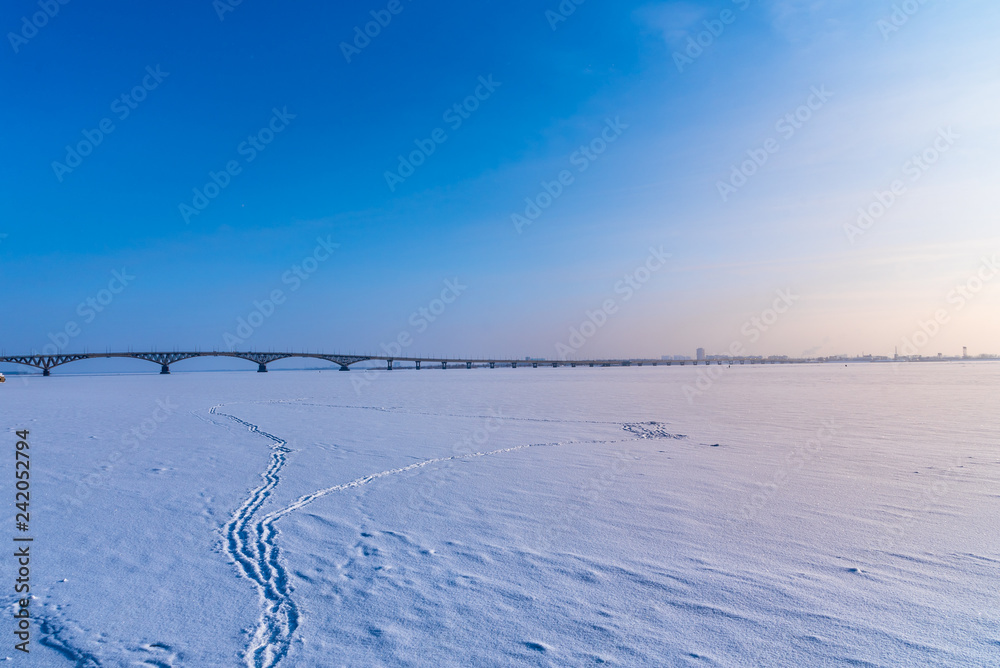 Sunset on the Volga in winter. Footprints in the snow and the Saratov Bridge