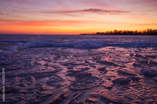 Winter landscape with frozen river and sunset fiery sky.