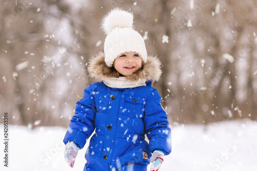 Happy laughing baby girl dressed in a blue thermal suit playing and running in a beautiful snowy winter park on Christmas