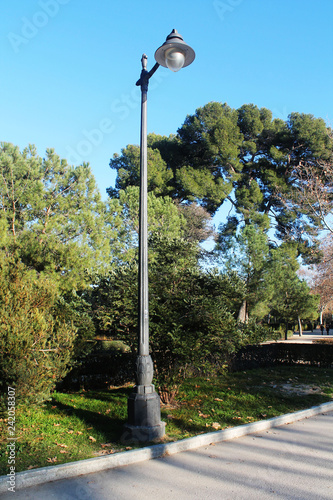 Gray metal street lamp, old construction, single bulb, located outdoors, surrounded by vegetation.