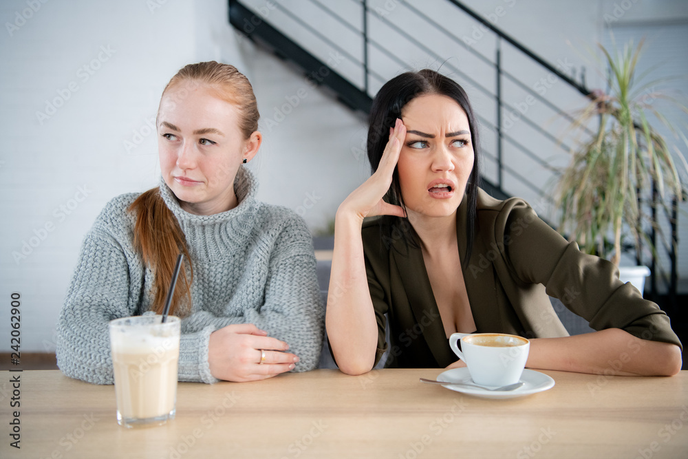 two girls young women sitting in a cafe with coffee cups, looking opposite direction. two girls young women sitting in a cafe with coffee cups, looking opposite direction.