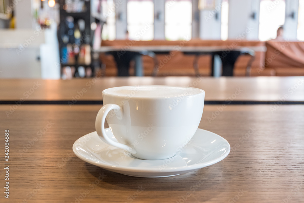 A cup of coffee with milk froth on wooden table in modern cafe A cup of coffee with milk froth on wooden table in modern cafe
