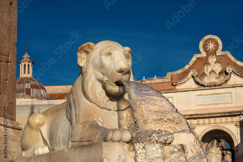 Marble egyptian lion from People Square central fountain with city wall ancient gate, in the background, in the center of Rome (erected in 1823)