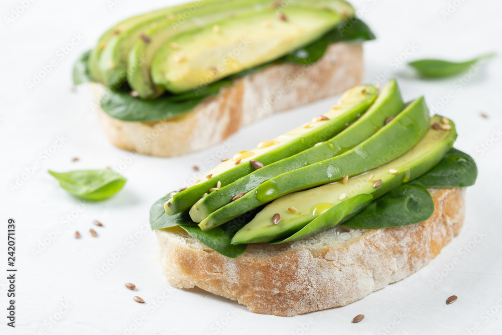 Two ciabatta toast with sliced avocado olive oil, spinach and flax and sesame seeds. Healthy vegetarian Breakfast on white background Two ciabatta toast with sliced avocado olive oil, spinach and flax and sesame seeds. Healthy vegetarian Breakfast on white background