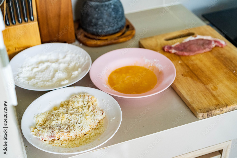 Cooking pork homemade cutlet in kitchen, pork chop on chopping board , and ingredient powder and egg on plate, preparing for fired pork. Cooking pork homemade cutlet in kitchen, pork chop on chopping board , and ingredient powder and egg on plate, preparing for fired pork.