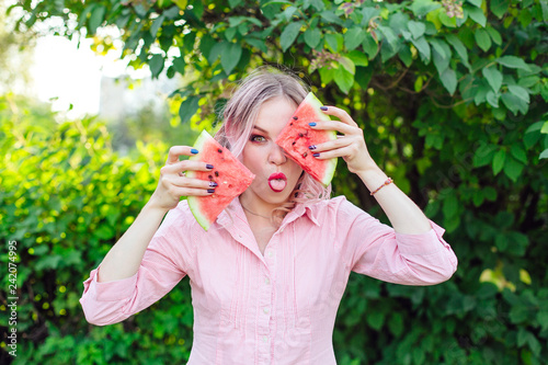 Beautiful young woman with pink hair holding two slices of watermelon in front of her face