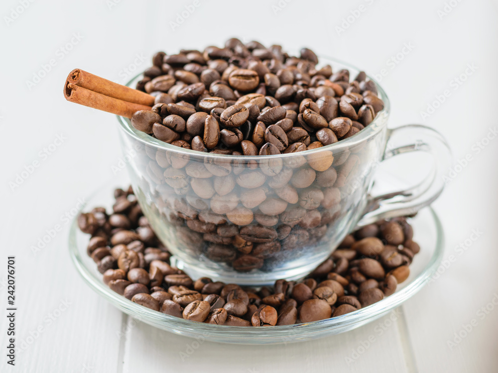 Glass bowl with coffee beans and cinnamon stick on white wooden table.