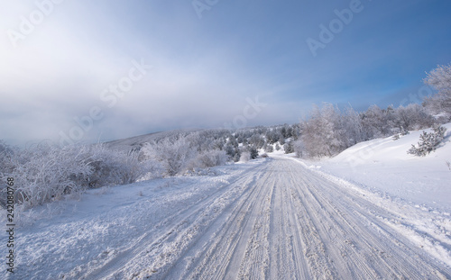 Mountain winter landscape, an icy road leading towards The Buzludzha Monument in Bulgaria. View of empty road with snow covered through a forested Mountain © mitzo_bs