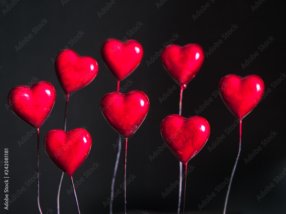 Glossy red hearts on sticks on dark background.