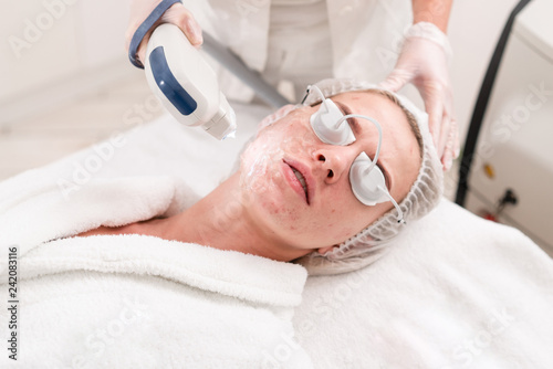 The doctor applies a special gel to the patient. Anti acne phototherapy with professional equipment. Beautiful woman during photo rejuvenation procedure. Face skin treatment at cosmetic clinic. photo