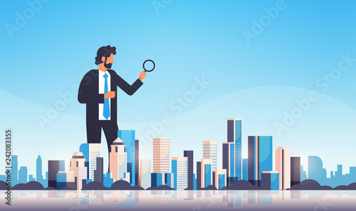 businessman holding magnifying glass search concept over big modern city building skyscraper cityscape skyline flat horizontal