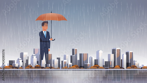 businessman holding umbrella at storm huge rain business protection concept over big modern city building skyscraper cityscape background flat horizontal