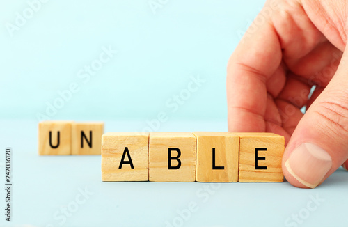 man hand spelling the text unable with wooden cubes, taking out the word un so it written able. success and challenge concept. photo