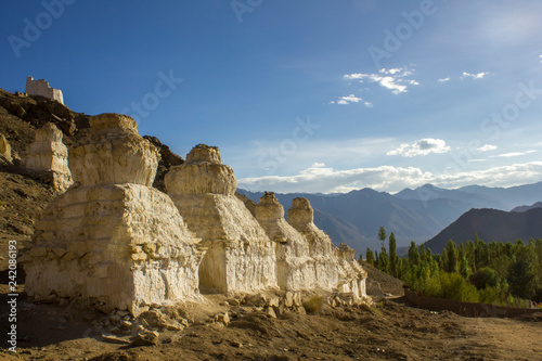 Tibetan Buddhist white temples of stupa on a stony hillside against the backdrop of a mountain valley under a blue sky and white clouds