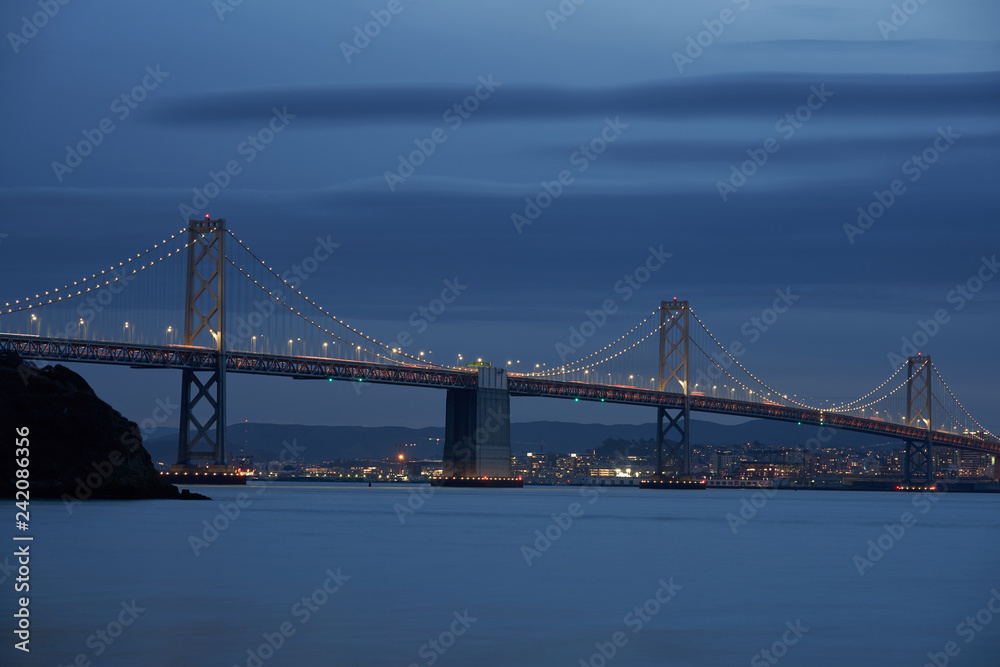 The San Francisco - Oakland Bay Bridge with San Francisco in the background during evening blue hour.
