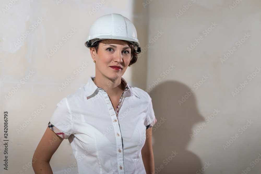 Cute young woman in white construction protection building helmet in unfinished apartment Cute young woman in white construction protection building helmet in unfinished apartment