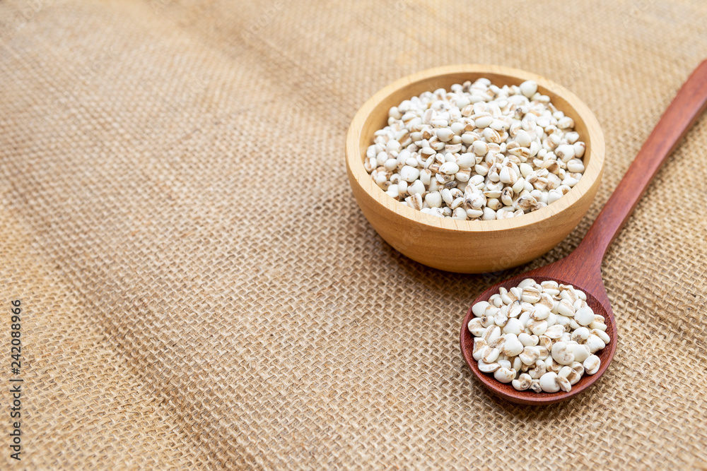 Raw organic Job's tears in wooden bowl and red wood spoon on hessian texture background Raw organic Job's tears in wooden bowl and red wood spoon on hessian texture background
