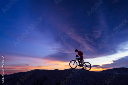 Cyclist riding mountain bike on the rocky trail at sunset.