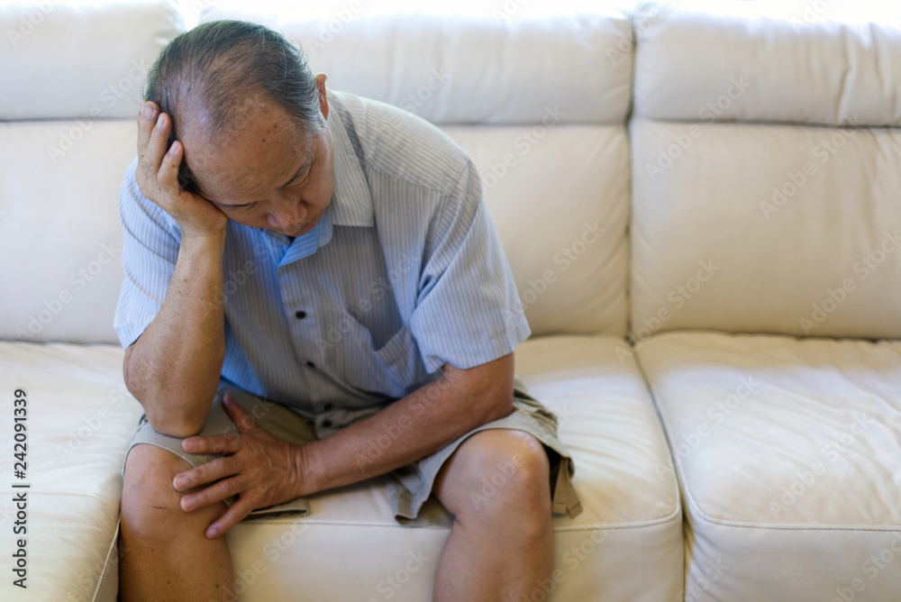 Close up view of Asian senior man suffering from headache, stress, migraine sitting alone on sofa at home. Unhappy retirement life. Senior health care and medical concern concept. Close up view of Asian senior man suffering from headache, stress, migraine sitting alone on sofa at home. Unhappy retirement life. Senior health care and medical concern concept.