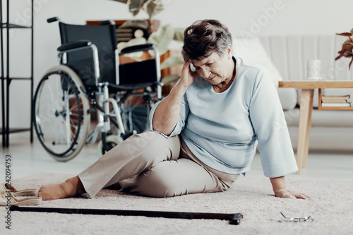 Disabled elderly woman with headache on the floor with walking stick photo