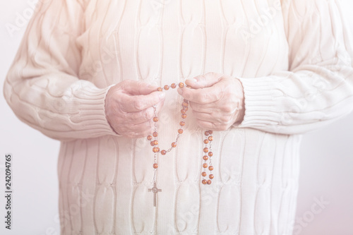Catholic senior person holding rosary with cross while praying in the church