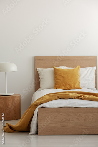 Yellow pillow and blanket on white bedding in simple hotel room with single bed, copy space on empty wall