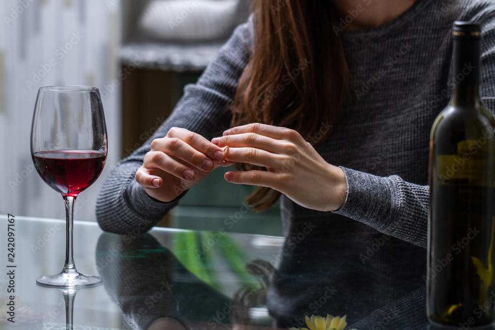 Divorced woman pulling wedding ring from finger and drinking a glass of