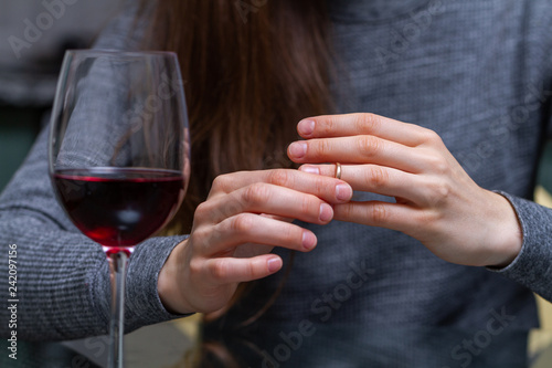 Divorced woman pulling wedding ring from finger and drinking a glass of a red wine because of adultery, betrayal and a failed marriage. Divorce concept. Relationship and love end. Life problems