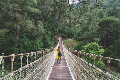 Woman with raincoat standing on suspension bridge.