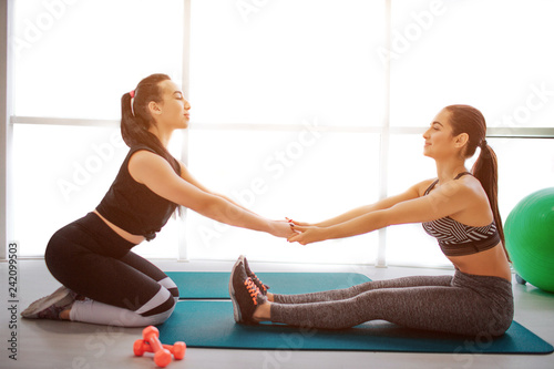 Well-built asian and european women help to stretch each others bodies. They hold hands in hands and concentrated on exercise. Uoung women stretching in fitness room. photo