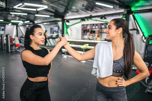 Young asian and european women stand in front of each other and hold hands together. They have rest after exercising. Woman on right have white tomwel on shoulder.