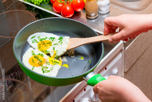 fried eggs on a griddle, hands with a wooden spatula close up